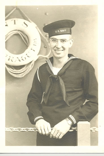 Smiling sailor wearing a U.S. Navy uniform beside a life preserver.