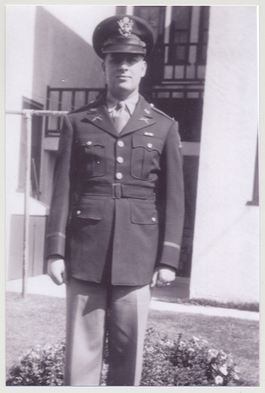 Serviceman standing outdoors in a military uniform and cap.