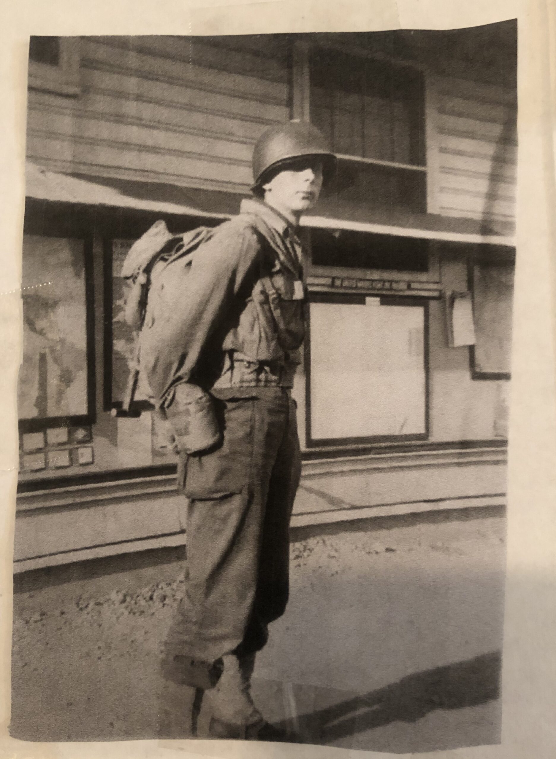Vernon Rieman standing outside a wooden building in military gear.
