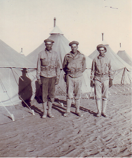 Three servicemen standing together outside military tents.