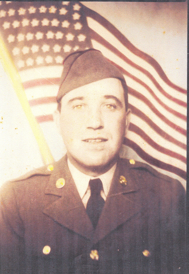 Serviceman wearing a military uniform and garrison cap in front of an American flag.