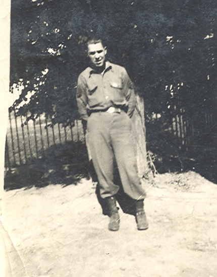 Serviceman standing outdoors in uniform near a wooden fence.
