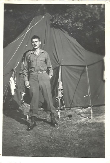 Serviceman standing outside a military tent in uniform.