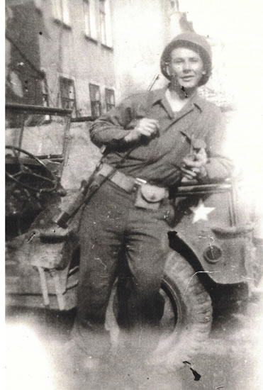 Serviceman seated outdoors in uniform while holding military equipment.