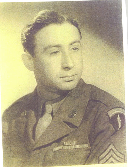 This is a sepia-toned photograph of a man in military attire. He is looking off to the side with a slight smile. His uniform includes a tie, and he is wearing what appears to be a medal or insignia on his chest.
