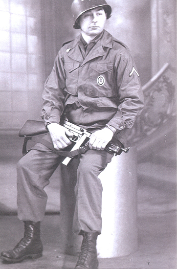 Serviceman seated in military gear while holding equipment in his lap.