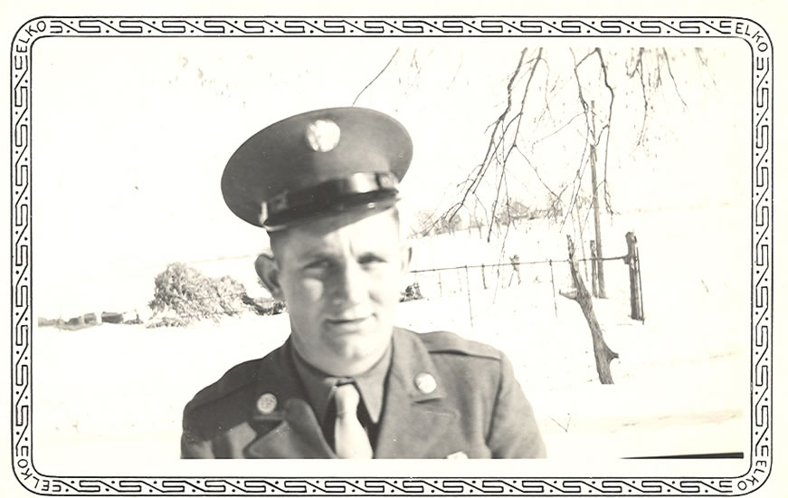 Serviceman standing outdoors in a military uniform and peaked cap.