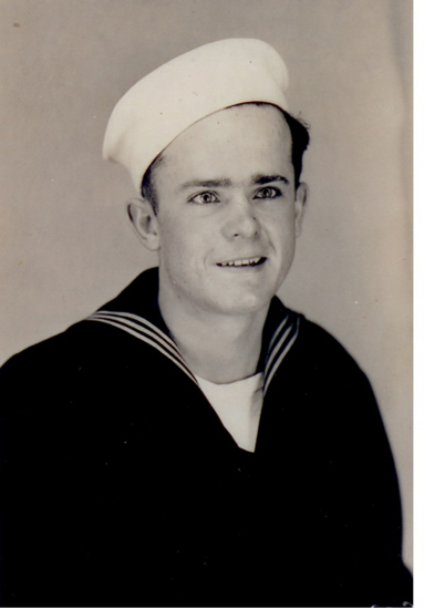 Sailor wearing a dark U.S. Navy uniform and white cap.