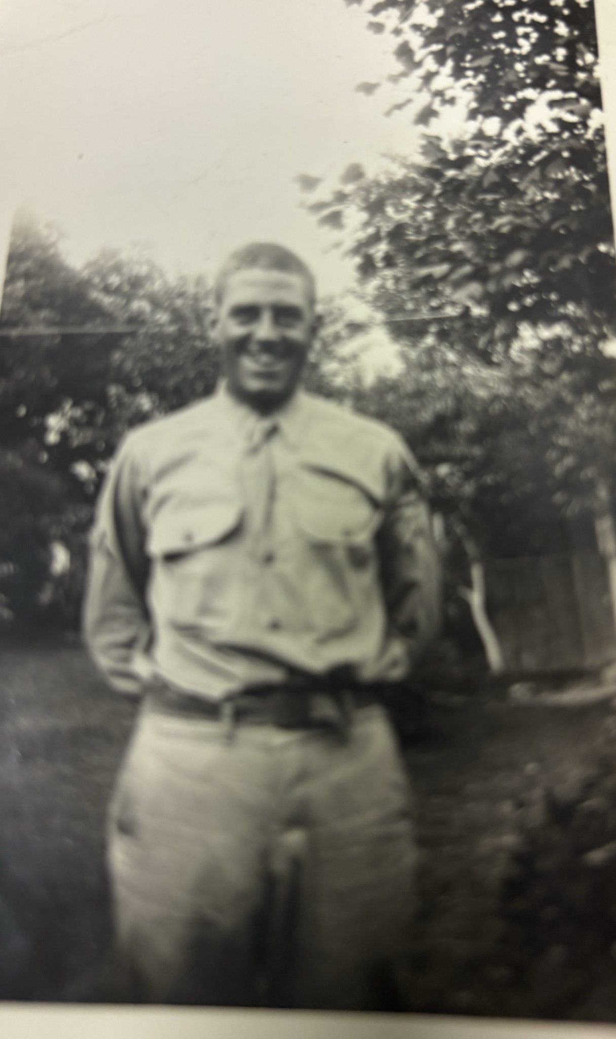 Black-and-white photo of a person standing upright in a military uniform. They are posing for the photograph, facing directly forward and smiling.