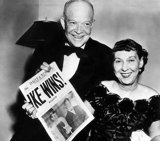 Dwight and Mamie Eisenhower smile while holding an “Ike Wins” sign.