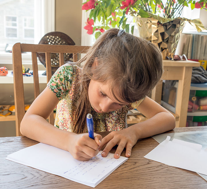 Young child writing a letter at a table.