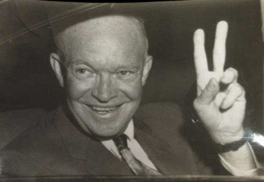 Dwight D. Eisenhower smiling and making a peace sign with his hand.