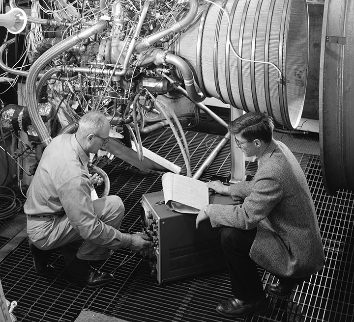 Engineers working beside complex machinery during the early space program.