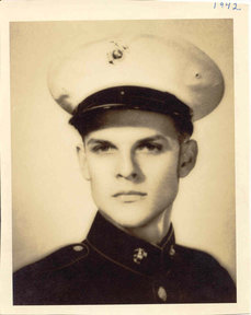 A military photograph features a young man dressed in a military uniform. He is wearing a hat while looking directly at the camera. The background is neutral, focusing attention on him.