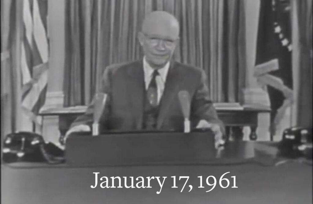 Black-and-white image of President Dwight D. Eisenhower delivering his farewell address on January 17, 1961, seated at a desk with microphones and American flags behind him.